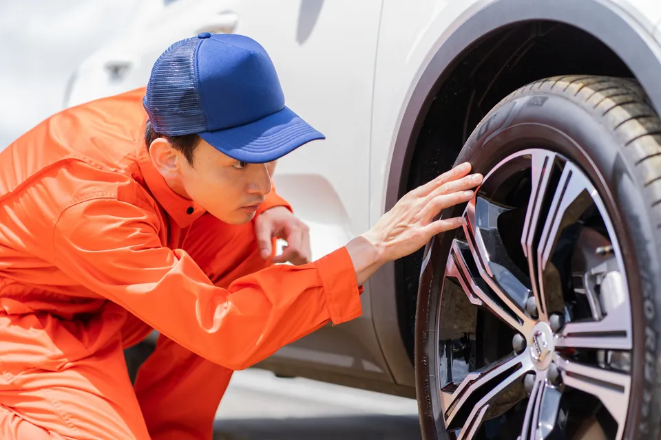 車のタイヤを点検するつなぎ姿の整備士