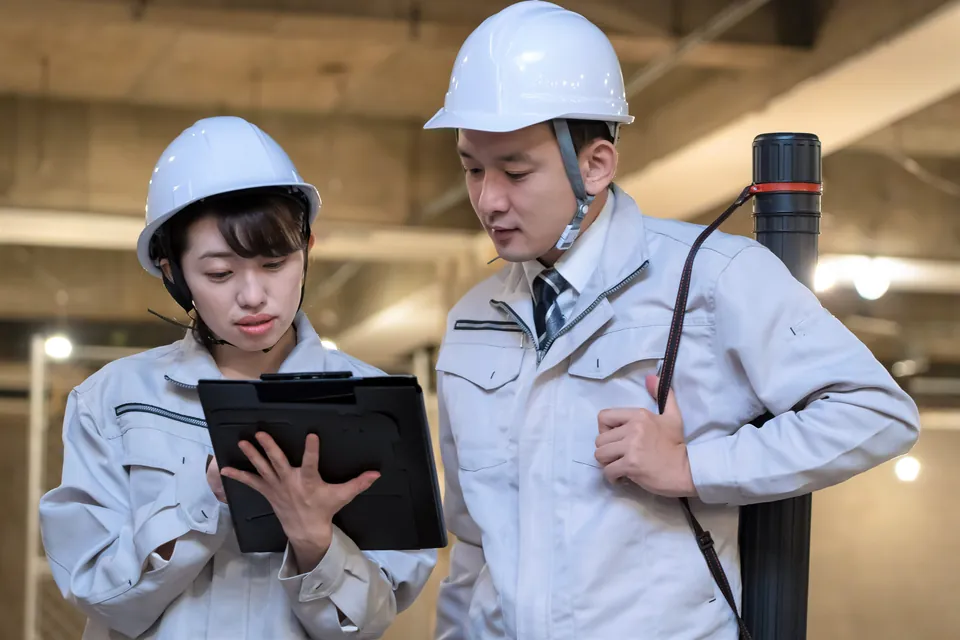 ヘルメットをかぶった2人がタブレットの画面を確かめる場面
