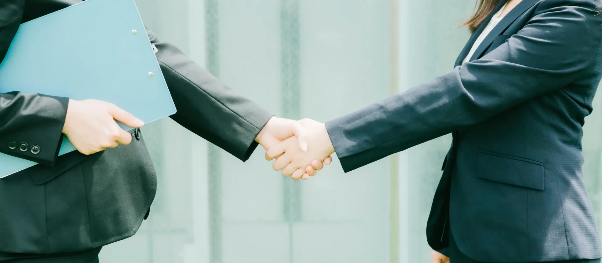 クリップボードを持つ担当者と事業者が握手する場面
